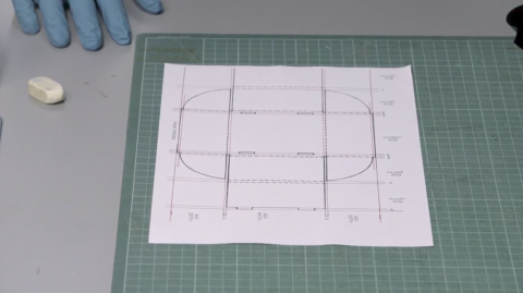 Caption: A box template with measured dimensions. A template for the base of a box with the measurements drawn on in pencil.