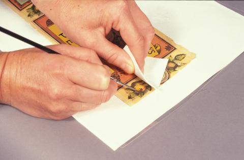 A person is using a damp paint brush a piece of paper to gently blot the surface of the label.