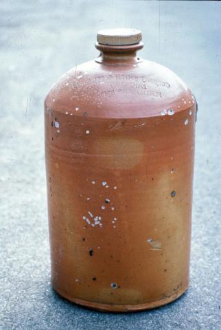 A small ceramic jar that has a flaked damaged surface caused by salt contamination.
